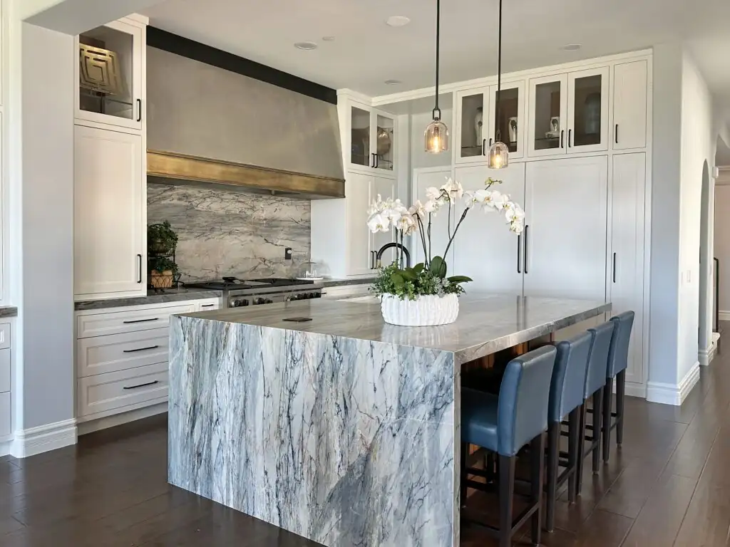 Kitchen remodeling Anaheim design-build project: white custom cabinets, blue-veined marble waterfall island, metal range hood and glass-front uppers in a Newport Coast kitchen