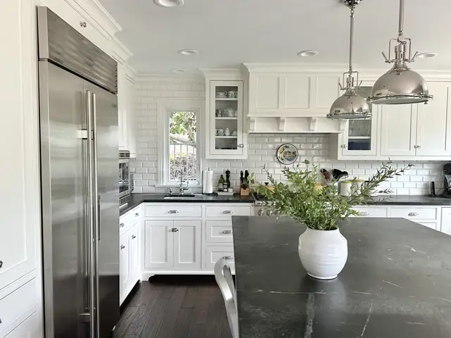 White kitchen with a soapstone island, industrial pendants, a stainless refrigerator and subway tile