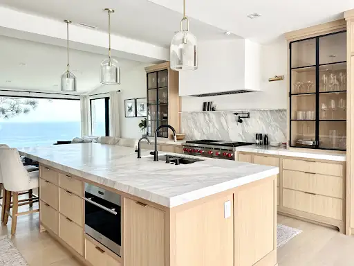 Laguna Beach kitchen remodel with light oak island, marble counters, black steel glass cabinets and large window